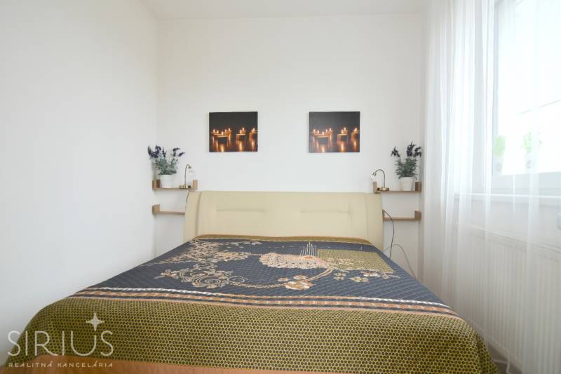 Hálószoba egy kétszobás lakásban világos ággyal és dekoratív képekkel a falon.