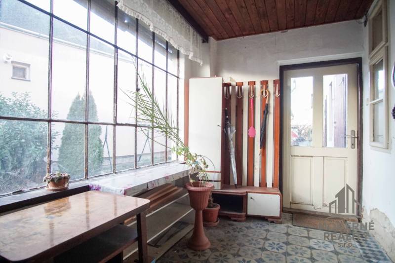 Családi ház belső tere virágcseréppel, asztallal és esernyőtartóval.