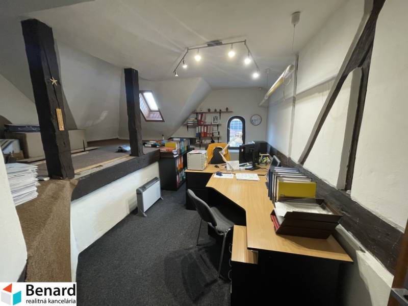 Iroda egy épületben, fa gerendákkal, íróasztalokkal és irodai kellékekkel felszerelve.