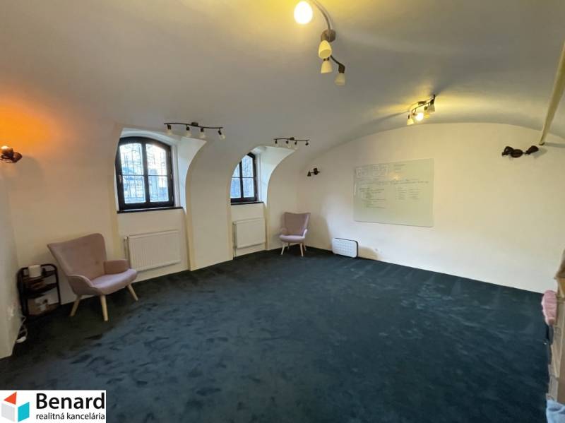 Az épület belső tere íves ablakokkal, zöld szőnyeggel és fali táblával.