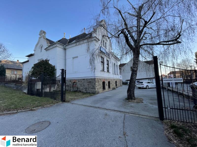 Épület a Vajanského utcában, Eperjesen, fával és parkoló autókkal.