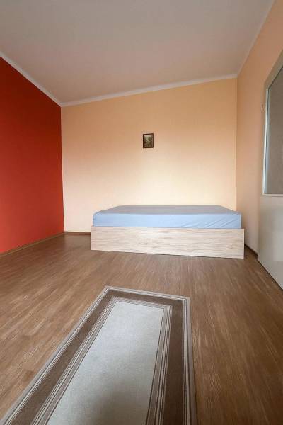 Szoba egy családi házban, fa dekorációjú padlóval, ággyal és piros fallal.