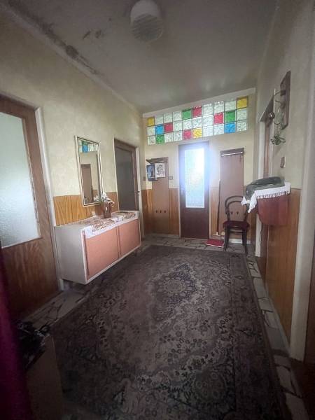 A családi ház folyosóján szőnyeg van, és az ajtók felett színes üvegablakok találhatók.