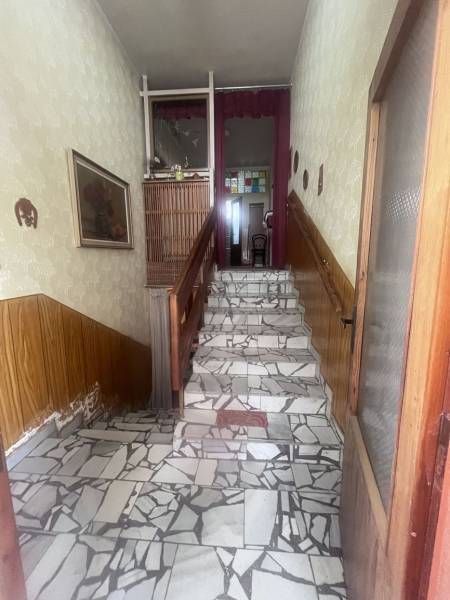 Mozaikás padlójú lépcsőház, fa korláttal és díszes tapétával egy családi házban.