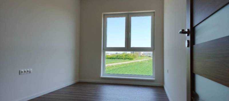 Világos szoba egy háromszobás lakásban fa mintázatú padlóval és nagy ablakkal.