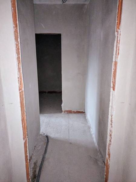 Keskeny folyosó egy építés alatt álló családi házban, a padlón feltárt kábelezéssel.