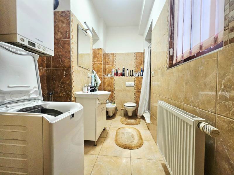 Fürdőszoba mosógéppel, mosdóval, WC-vel és világos kerámia csempével egy háromszobás lakásban.