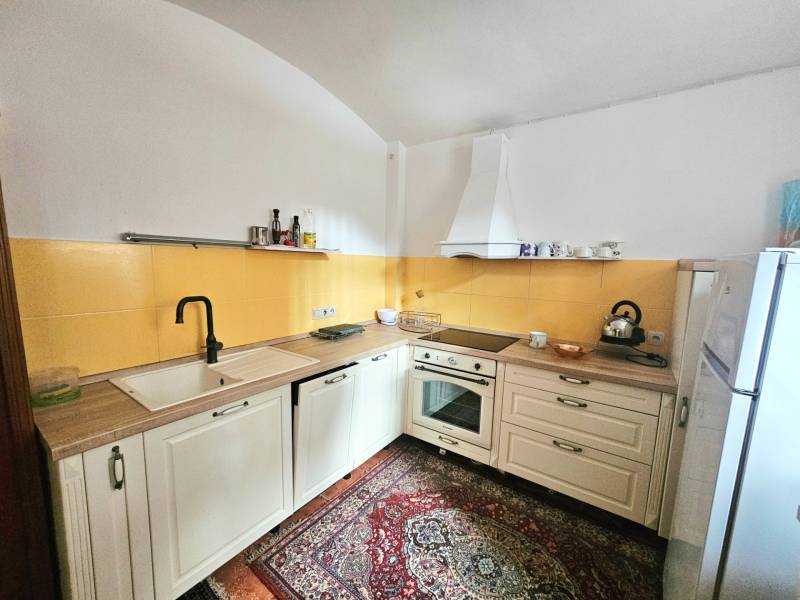 Konyha egy háromszobás lakásban krémszínű szekrényekkel, sárga csempével és mintás szőnyeggel.