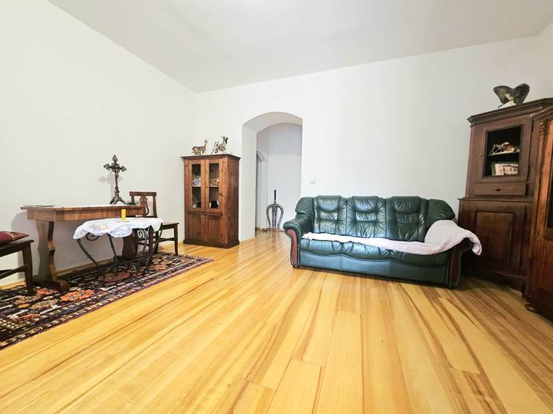 Nappali egy háromszobás lakásban, fa dekorációjú padlóval, kanapéval és fa bútorokkal.