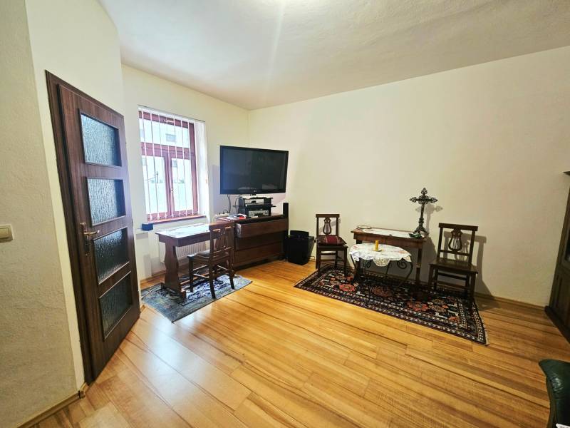 Szoba egy háromszobás lakásban, fa mintázatú padlóval és tévével az asztalon.