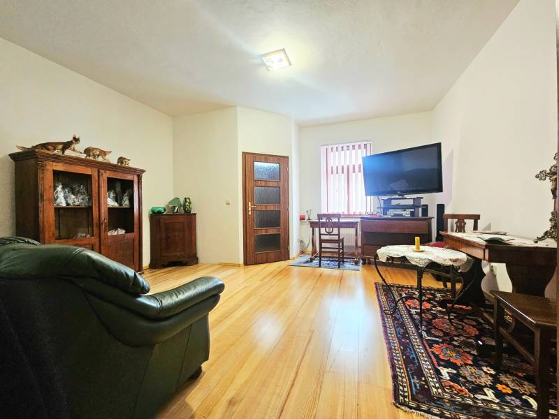 Nappali egy háromszobás lakásban, fa dekorációjú padlóval, kanapéval és televízióval felszerelve.