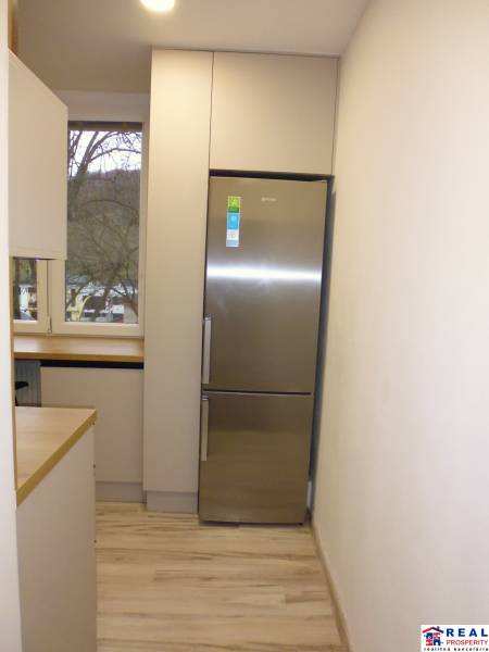 Konyha fa hatású padlóval és hűtőszekrénnyel egy kétszobás lakásban.