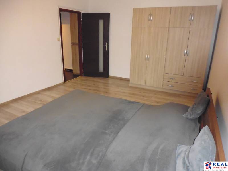 Hálószoba egy kétszobás lakásban fa mintázatú padlóval, ággyal és ruhásszekrénnyel.