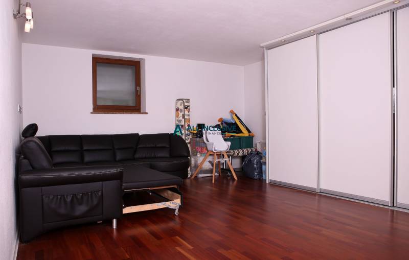 Családi ház fekete kanapéval, fehér szekrényekkel és fa mintázatú padlóval.