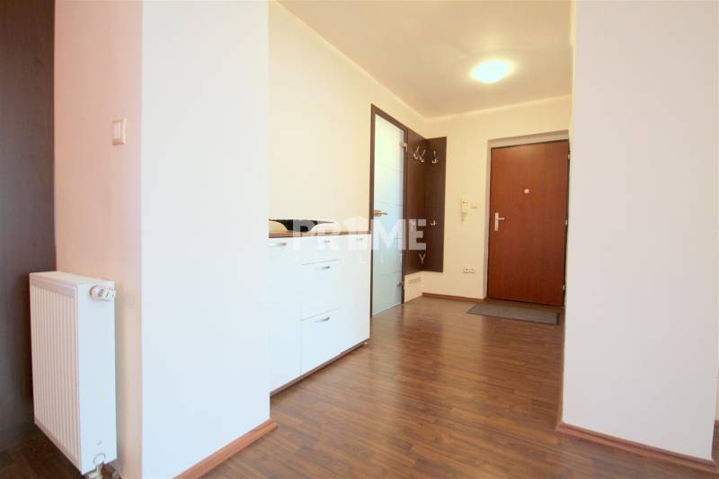 Előszoba egy kétszobás lakásban, fa mintázatú padlóval, fehér komóddal és függő akasztókkal.