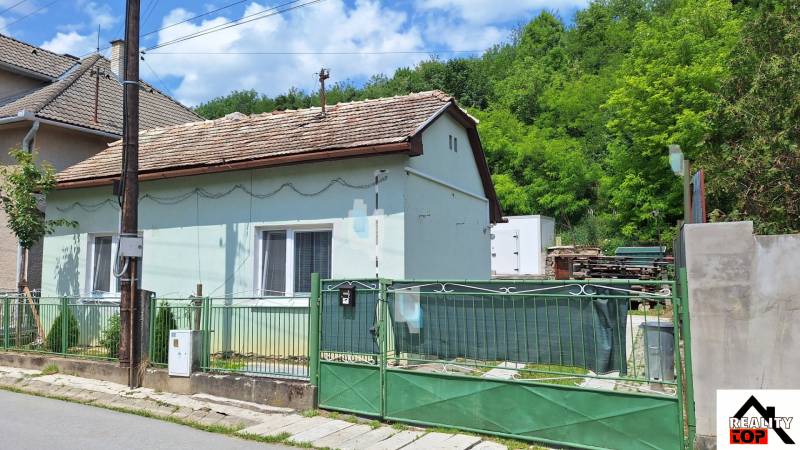 Családi ház Ajnácskőn, egyszintes kialakítással, fedett tetővel és zöld kerítéssel.