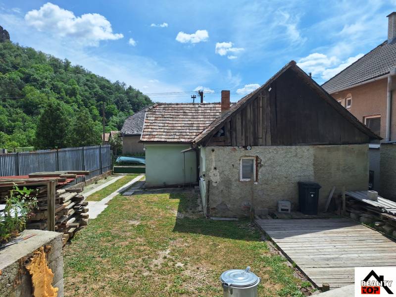 Családi ház Ajnácskőn bekerített udvarral, fa melléképülettel és tárolt fával.