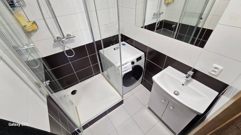 Fürdőszoba mosógéppel, zuhanyzóval és mosdóval egy háromszobás lakásban.