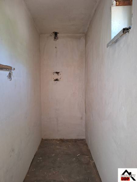 Szűk belső tér egy családi házban kis ablakkal és betonpadlóval.