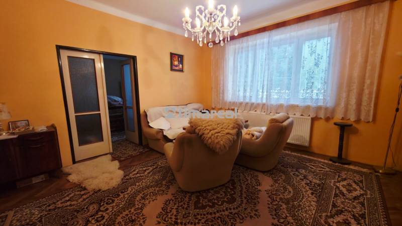 Nappali egy családi házban szőnyegekkel, csillárral és kényelmes fotelekkel.