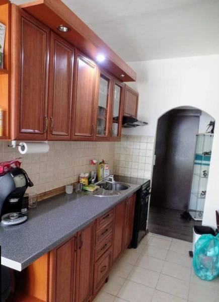 Konyha egy háromszobás lakásban, fa szekrényekkel és csempézett fallal a munkalap felett.