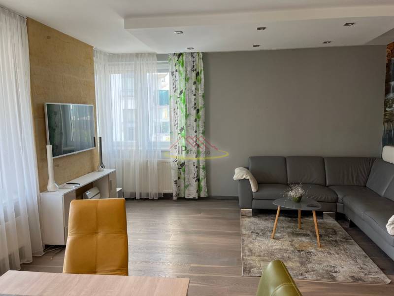 Nappali egy négy szobás lakásban, fa dekor padlóval, szürke kanapéval és TV-vel.