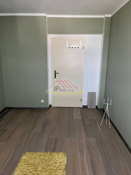 Hely egy 4 szobás lakásban fa mintázatú padlóval és zöld fallal.