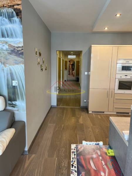 Nappali egy négy szobás lakásban, fa mintázatú padlóval és konyhabútorral.