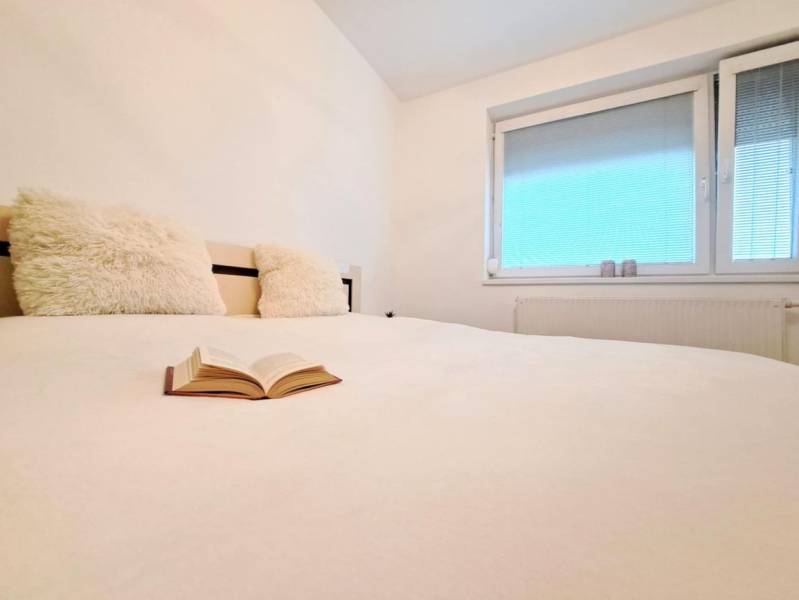 Ágy kilátással, nyitott könyvvel és ablakkal egy kétszobás lakásban.