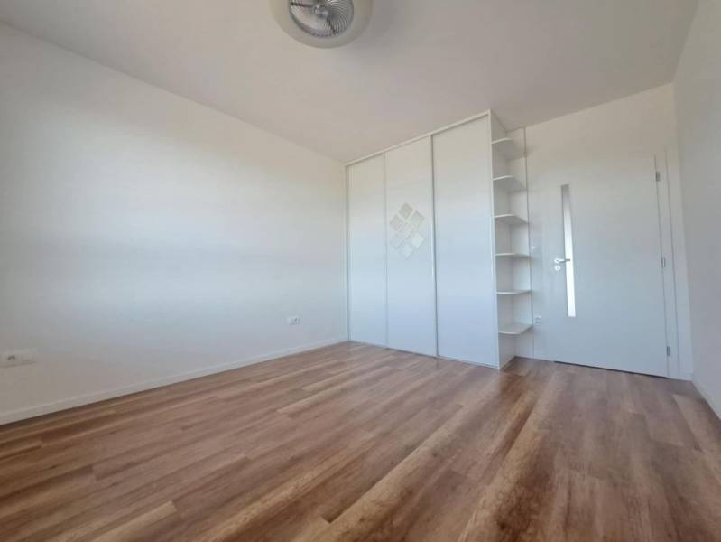 Szoba egy kétszobás lakásban fa dekorációjú padlóval, fehér szekrénnyel és polcokkal.