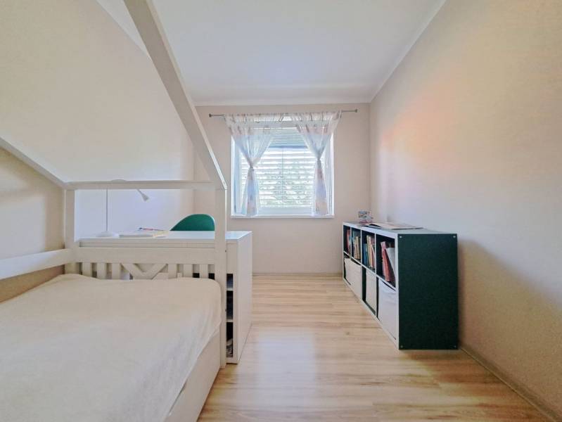 Családi ház szobája ággyal, könyvespolccal és fa dekorációjú padlóval.