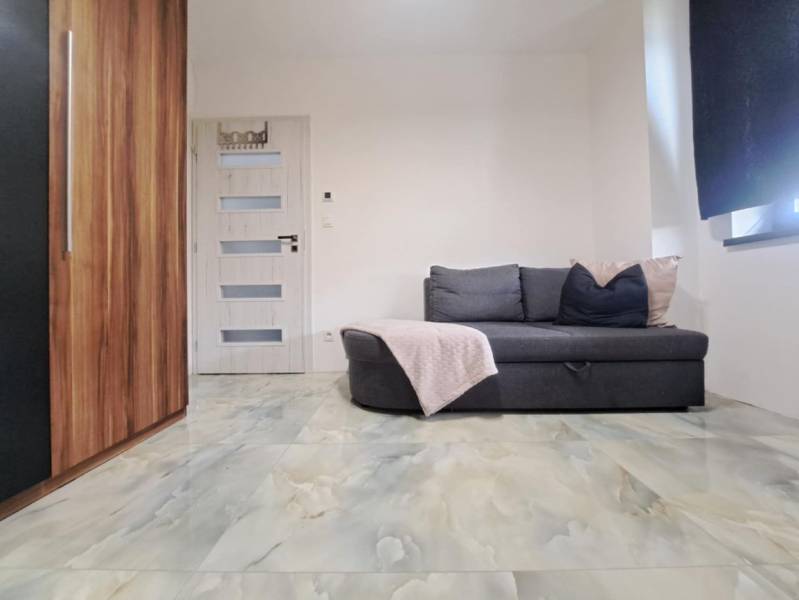 Egy családi ház szobája kanapéval, szekrénnyel, ajtóval és márvány mintás padlóval.