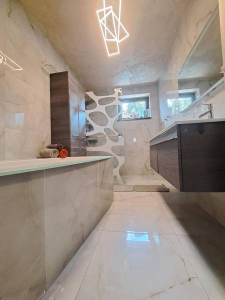 Fürdőszoba családi házban káddal, modern világítással, csempével és mosdóval.