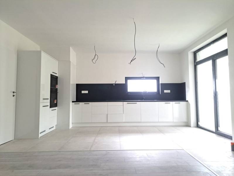 Konyha egy családi házban, fa dekor padlóval, fehér szekrényekkel és beépített készülékekkel.