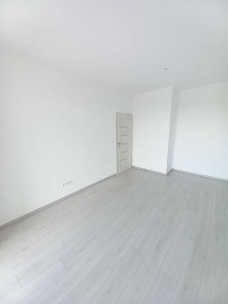 Szoba egy kétszobás lakásban fehér falakkal és fa dekorációjú padlóval.