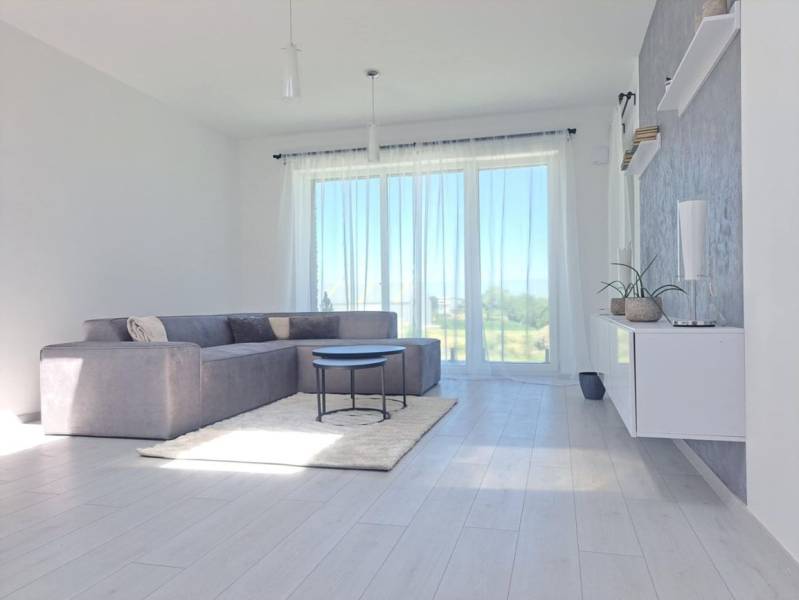 Világos nappali egy kétszobás lakásban nagy ablakokkal és fa mintázatú padlóval.