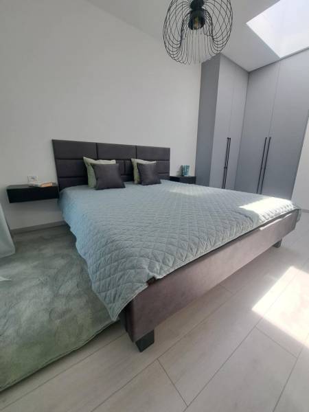 Hálószoba nagy ággyal, szürke szekrényekkel és fekete csillárral egy kétszobás lakásban.