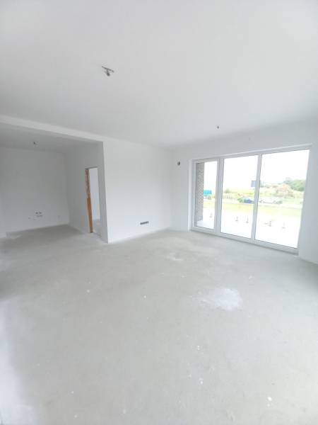 Világos nappali egy kétszobás lakásban nagy ablakokkal és üres padlóval.