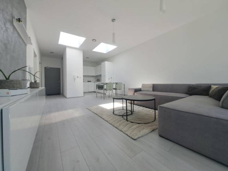 Nappali kanapéval, fa dekor padlóval és étkezőasztallal egy kétszobás lakásban.