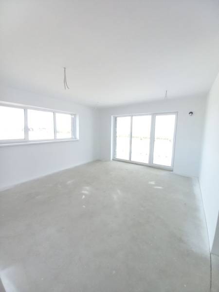 Tágas szoba egy kétszobás lakásban világos falakkal és nagy ablakokkal.