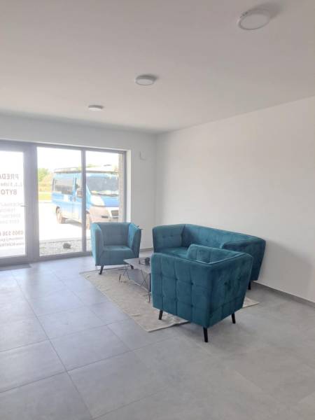 Kereskedelmi helyiségek türkiz ülőbútorokkal, szürke padlóval és nagy ablakkal.