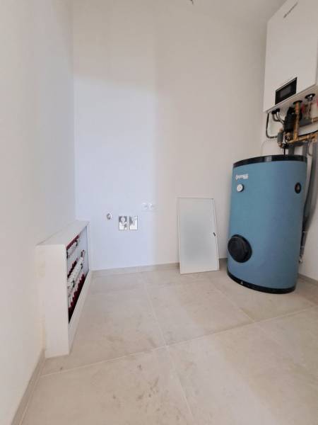 Kazánház családi házban, bojlerekkel és vezetékekkel világos padlón.