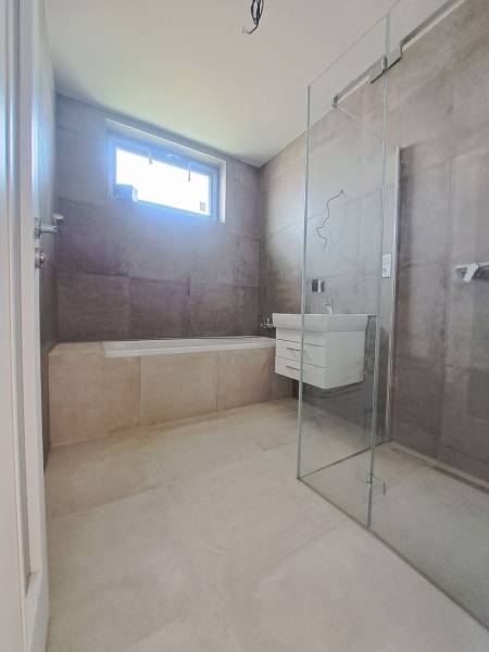 Családi ház fürdőszobája káddal, zuhanyzóval és mosdóval.