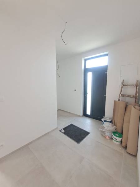 Családi ház előszobája járólappal, az ajtó mellett lépcső és anyag található.