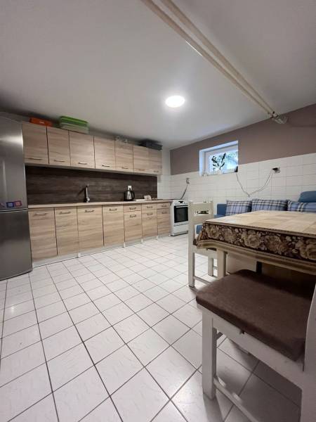 Konyha családi házban csempével, fa szekrényekkel, hűtőszekrénnyel és étkezőasztallal.