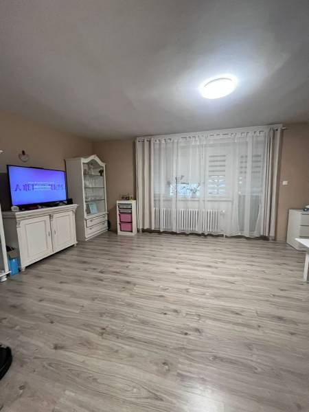 Szoba egy családi házban fa dekorációjú padlóval, televízióval és függönyökkel.