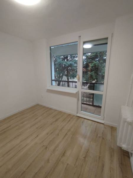 Szoba világos falakkal, fa mintázatú padlóval és kilátással a zöldre.