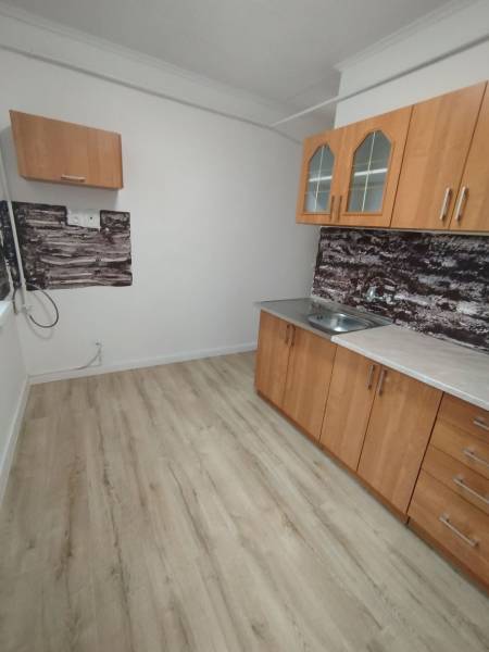 A háromszobás lakás konyhája fa dekor padlóval és egyszerű szekrényekkel rendelkezik.