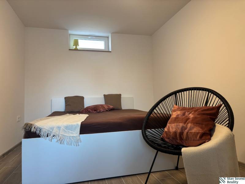 Hálószoba családi házban egyszerű ággyal és kényelmes fotellel.