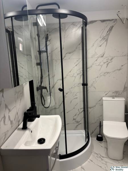 Családi ház fürdőszobája márványburkolattal, zuhanyzóval és mosdóval.